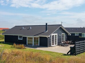 En toetagers bygning med et mørkt tag, en overdækket terrasse med udendørs møbler, og en klar himmel.