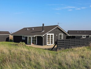 A residential building with a dark exterior, a sloped roof, and a fenced yard.