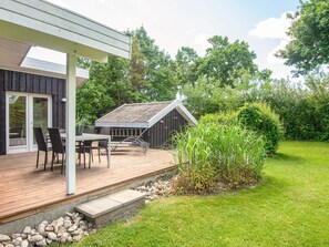 A wooden deck with a table and chairs, a small shed, and a grassy area with plants. - 6 Person Holiday Home in Hadsund (Hadsund)