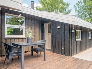A wooden deck with a table and chairs, a potted plant, and a window overlooking greenery. - 6 Person Holiday Home in Hadsund (Hadsund)