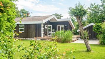 Et moderne hus med en terrasse, omgivet af frodig vegetation.