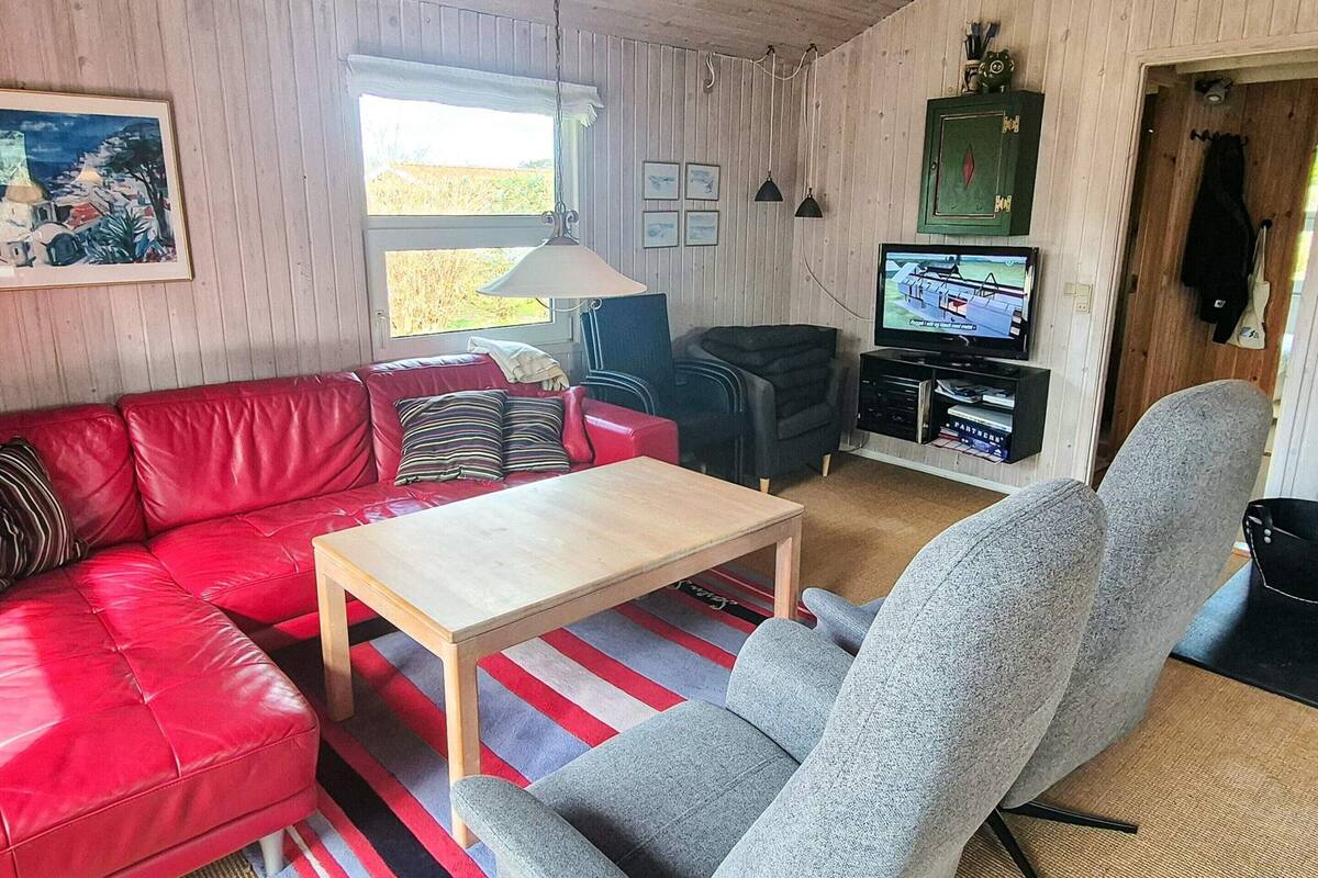 A cozy living room with a red leather sofa, a grey armchair, a wooden coffee table, and a television on a wooden cabinet.