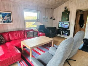 A cozy living room with a red leather sofa, a grey armchair, a wooden coffee table, and a television on a wooden cabinet. - 6 Person Holiday Home in Hadsund (Hadsund)