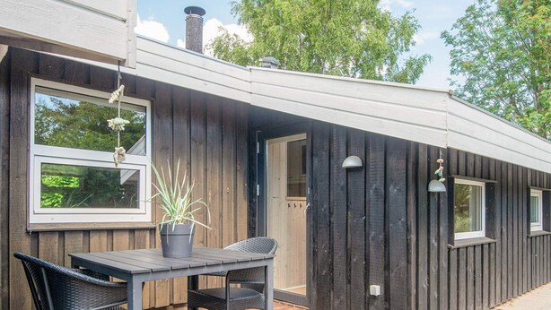 A wooden deck with a table and chairs, a potted plant, and a window overlooking greenery. - 6 Person Holiday Home in Hadsund (Hadsund)