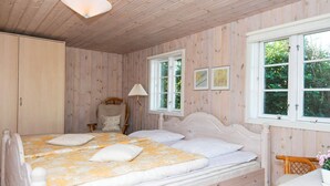 A bedroom with a double bed, wooden walls, a chair, and a window. - Premium Holiday Home in FanÃ¸ near Beach (Fano)