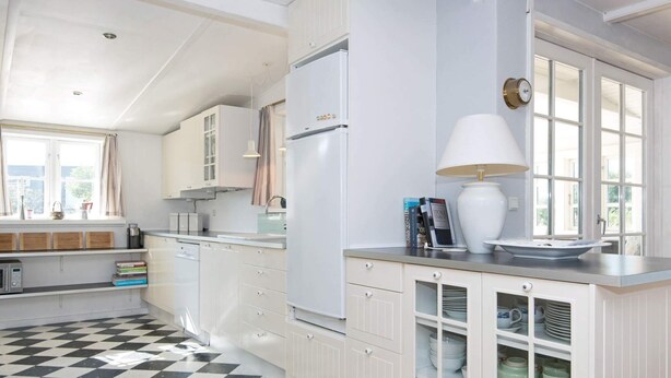 A kitchen with white cabinets, a black and white checkered floor, and a window with curtains. - Premium Holiday Home in FanÃ¸ near Beach (Fano)