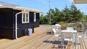 A wooden deck with outdoor seating, a black building with white windows, and a utility pole in the background. - Premium Holiday Home in FanÃ¸ near Beach (Fano)