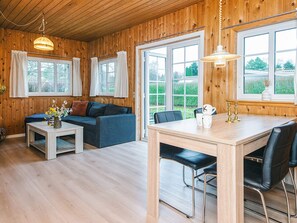 A cozy room with wooden walls, a sofa, a dining table with chairs, and large windows. - 4 Person Holiday Home in Ansager (Ansager)