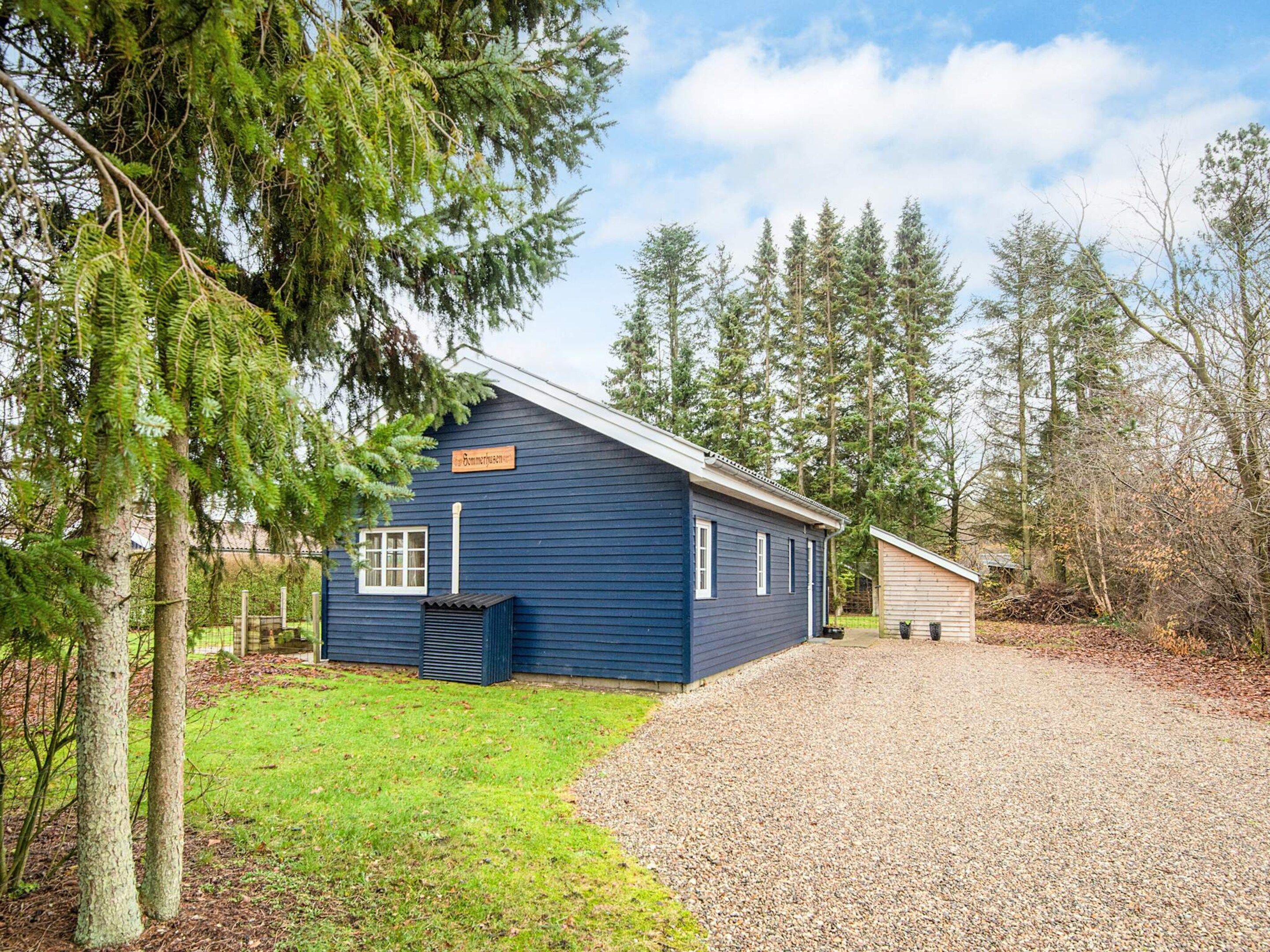 A single-story blue building with a gravel driveway, surrounded by trees and a grassy area.