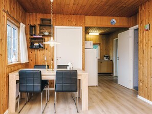 A wooden interior with a dining area featuring a table and chairs, a kitchen with appliances, and a door leading to another room. - 4 Person Holiday Home in Ansager (Ansager)