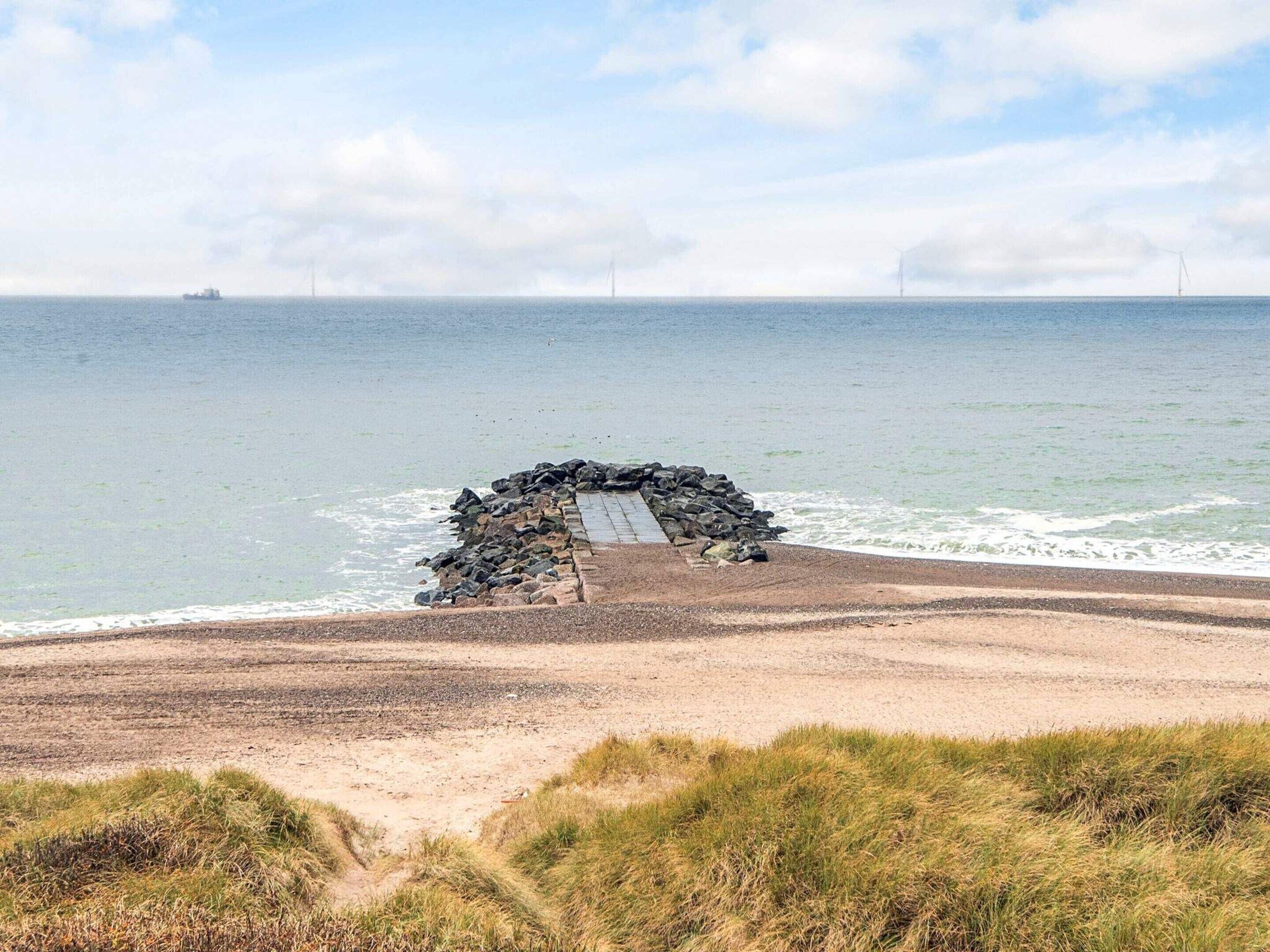 A beach with a rocky structure and a paved path leading to the water.