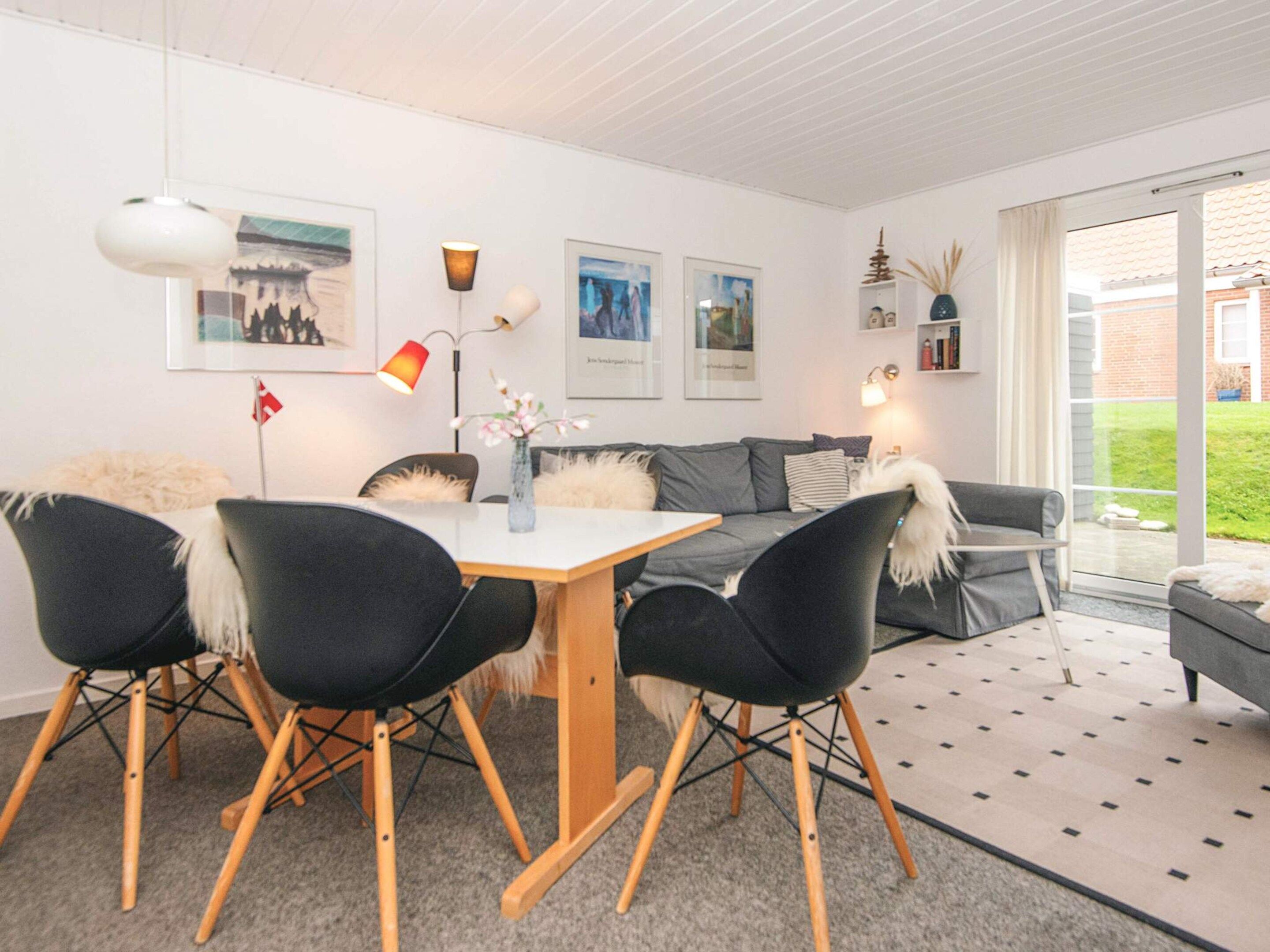 A modern living room with a dining area, featuring a sofa, chairs, a table, and artwork on the walls.