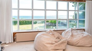 Quarto com uma janela ampla de frente para um jardim e o mar, um radiador e duas poltronas de feijão.