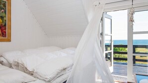 Quarto com cama, janela com vista para o mar e um quadro na parede.
