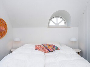 A bedroom with a bed, two bedside lamps, a window, and a wall decoration.