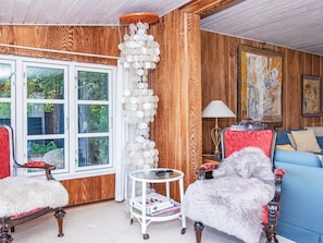 A room with wooden paneling, a white chair, a blue sofa, a small round table, and a large window.