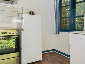 A kitchen with a white refrigerator, a stove, and a window with blue curtains. - Lovely Holiday Home in Jutland near Beach (Ebeltoft)