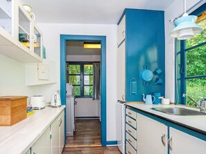 A compact kitchen with white cabinets, a wooden countertop, and a window with curtains.