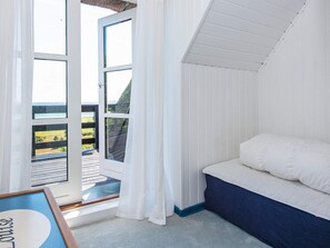 A room with a bed, a window with curtains, and a view of a green landscape.