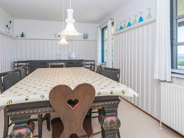 A dining room with a large table, chairs, a hanging light fixture, and a window with curtains.