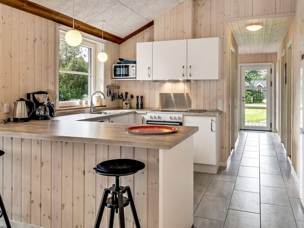 A kitchen with wooden paneling, a central island with stools, a stove, and a microwave.