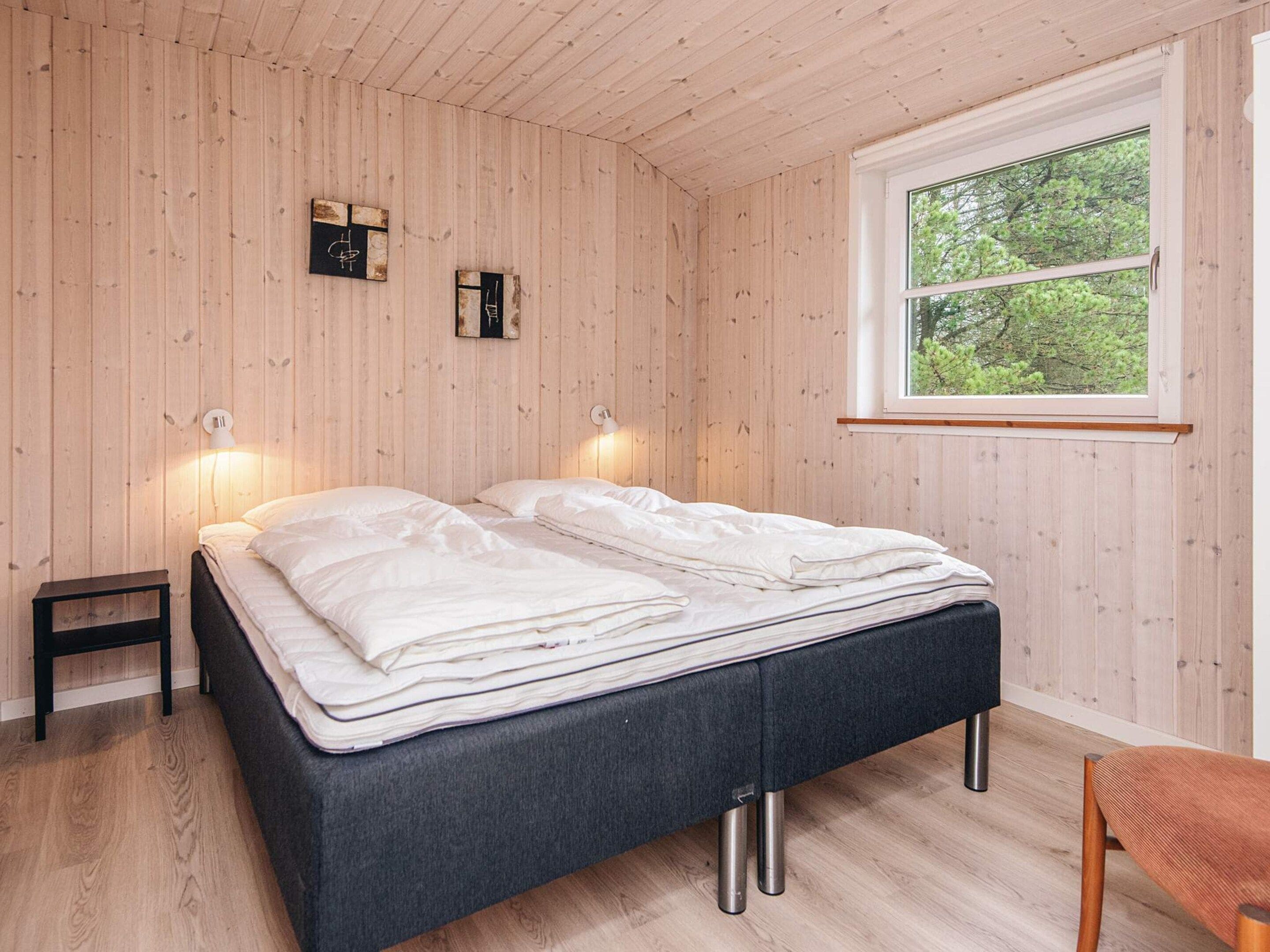 A bedroom with a bed, bedside lamps, a small table, and a window with a view of trees.