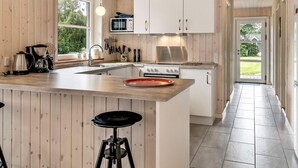 A modern kitchen with wooden paneling, a large island with stools, a stove, and a microwave. - 4 Star Holiday Home in Oksbol (Oksbol)