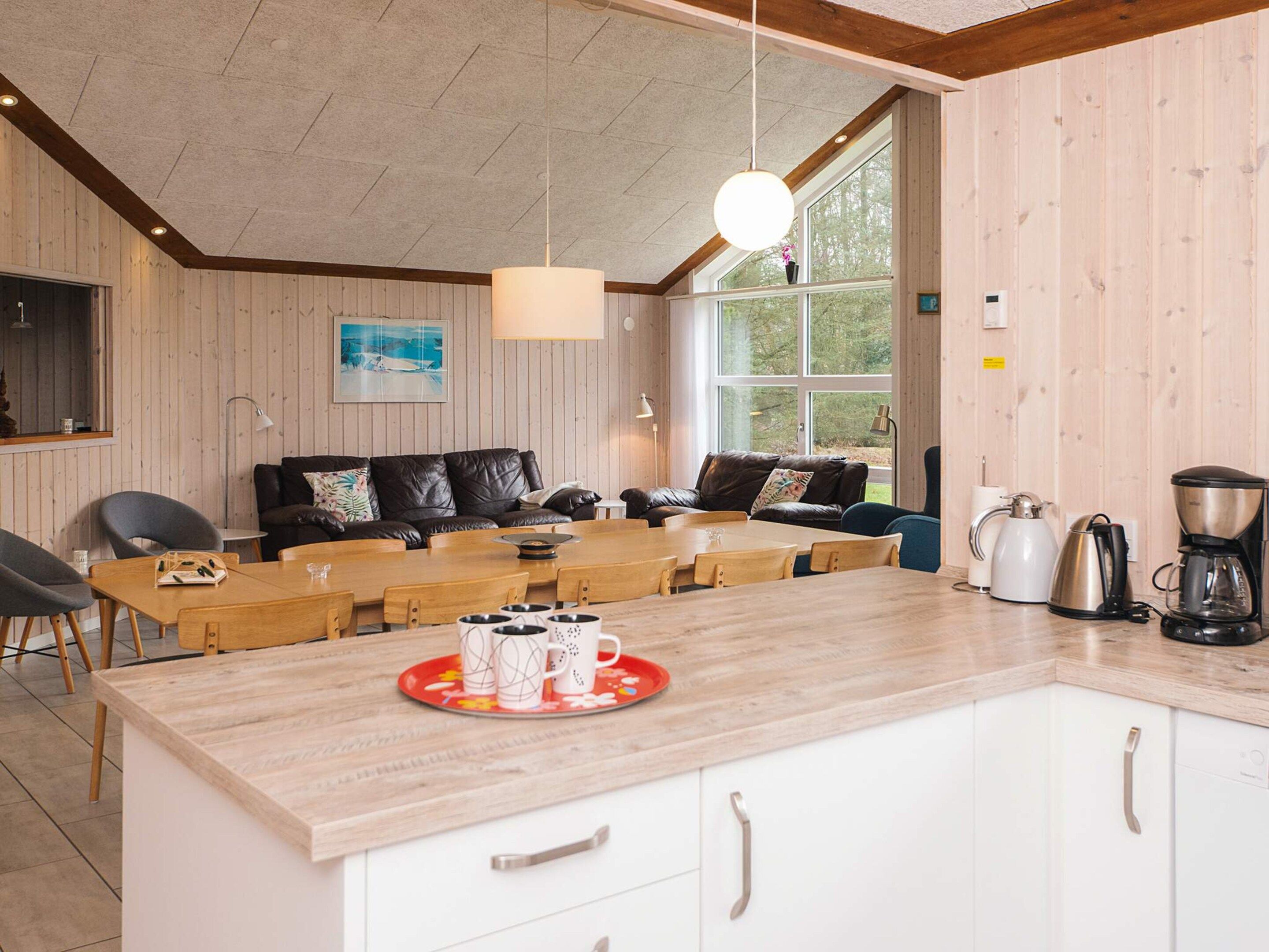 A cozy room with a wooden ceiling, a sofa, a dining table with chairs, and a kitchen area with a coffee maker.