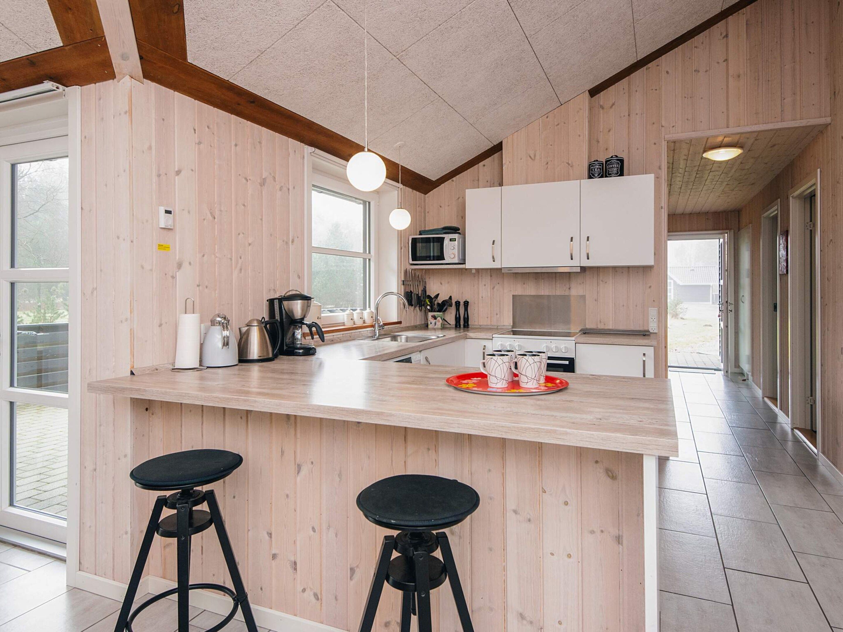 A modern kitchen with wooden paneling, a central island with stools, a microwave, and a stove.