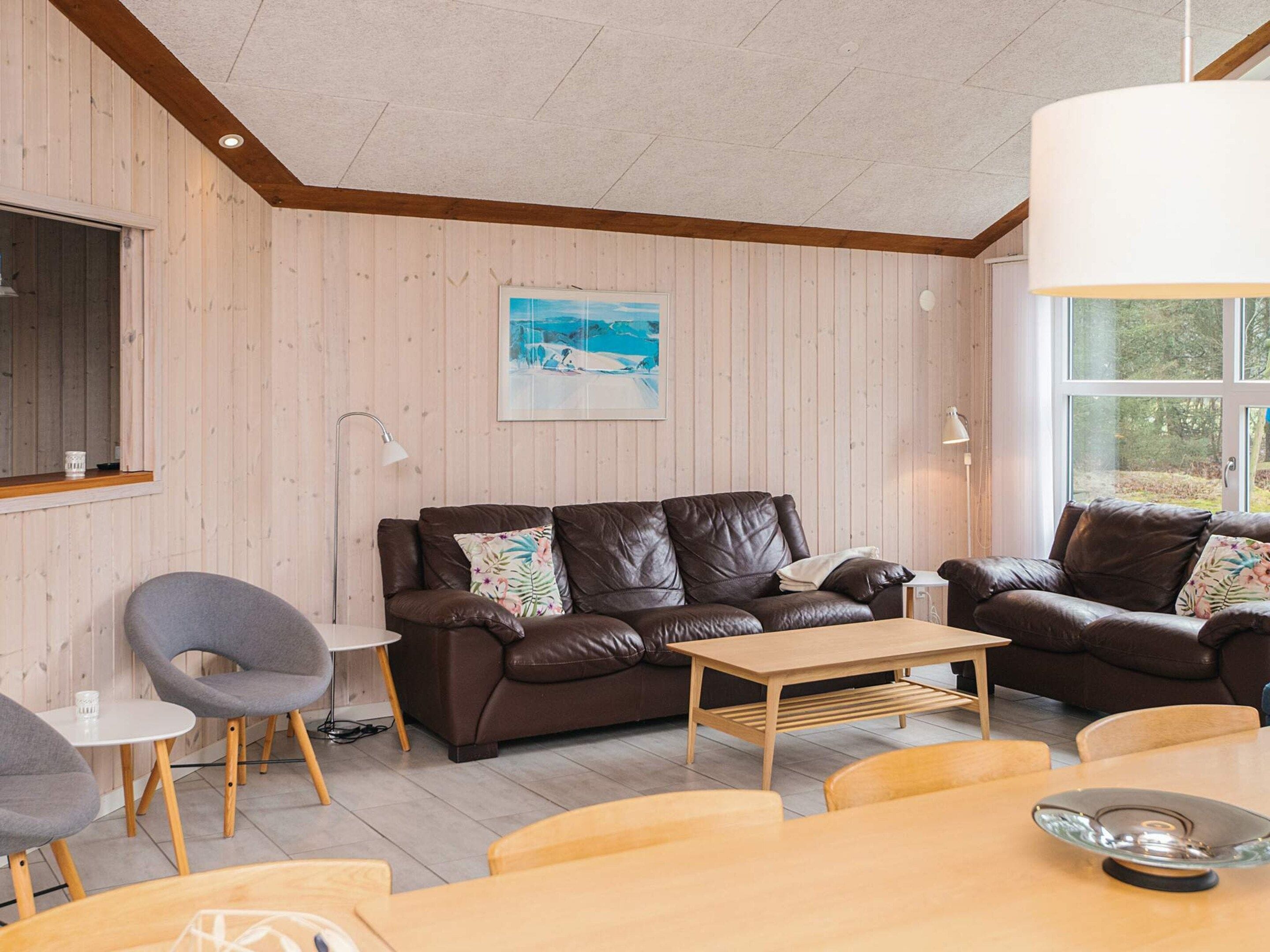 Una sala de estar acogedora con paredes de madera, un sofá de cuero marrón, una mesa de centro de madera y una mesa de comedor con sillas.