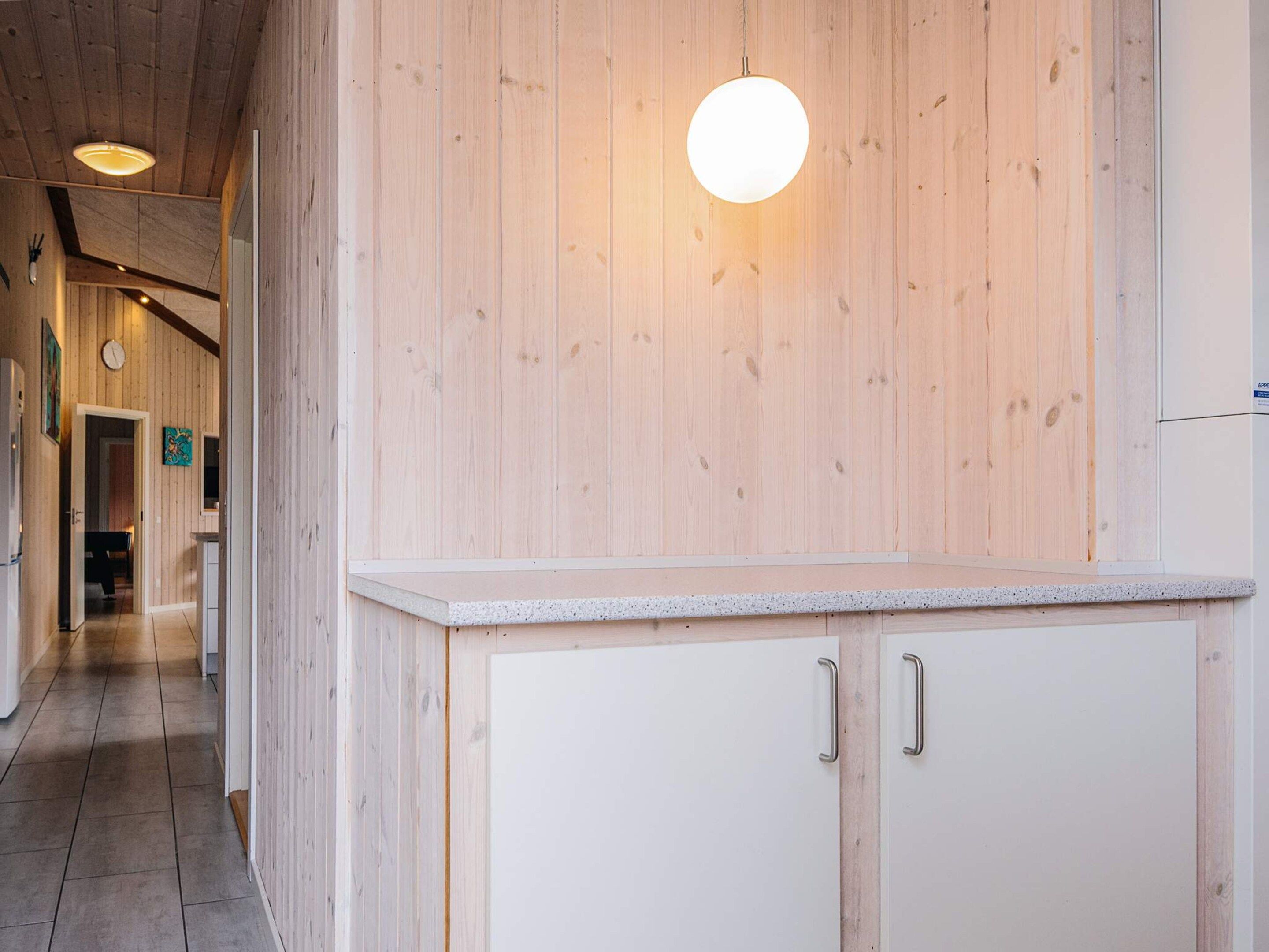 A hallway with wooden walls, a white cabinet with two handles, and a round light fixture.