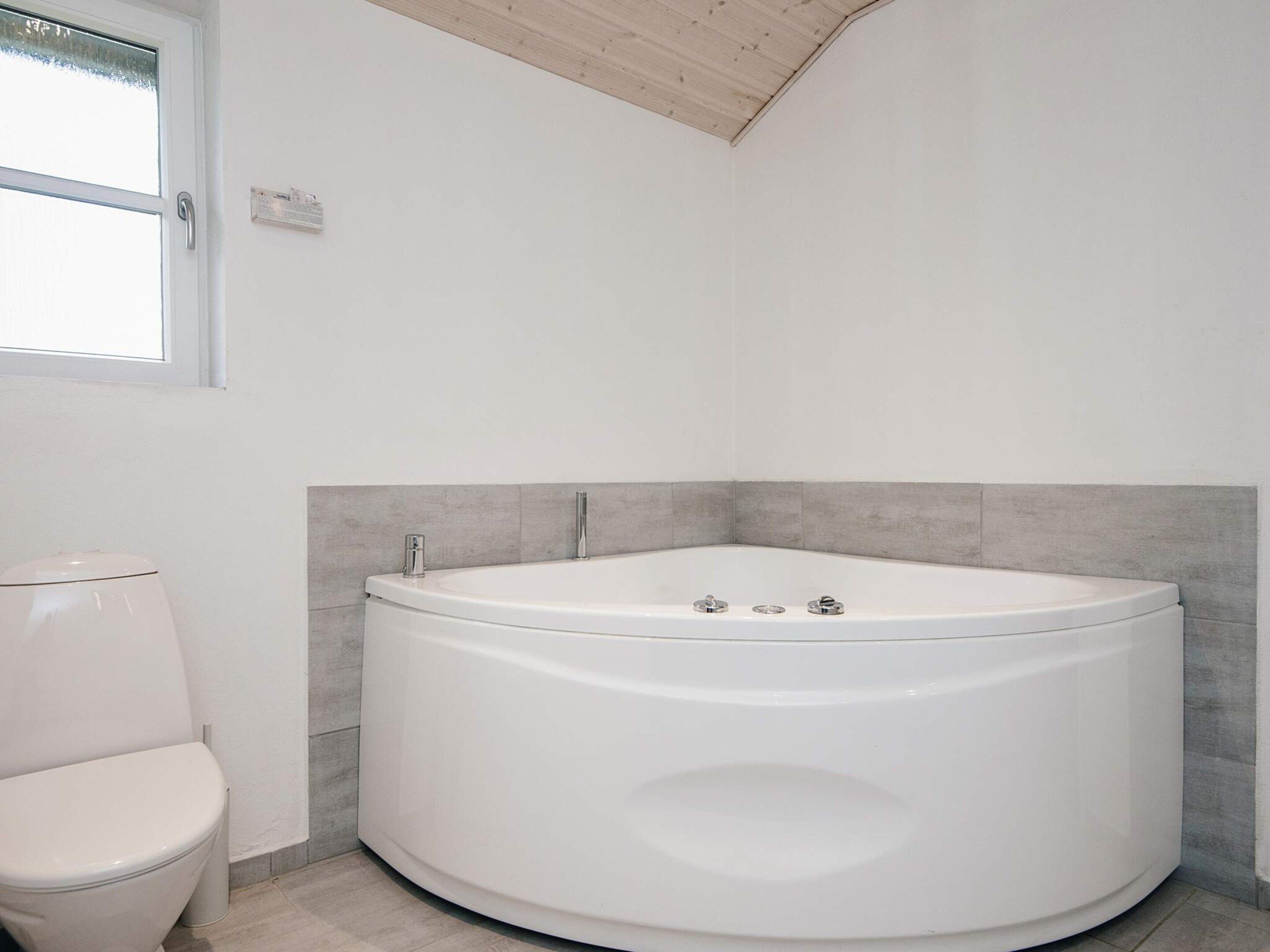 A modern bathroom with a freestanding bathtub, a toilet, and a window.