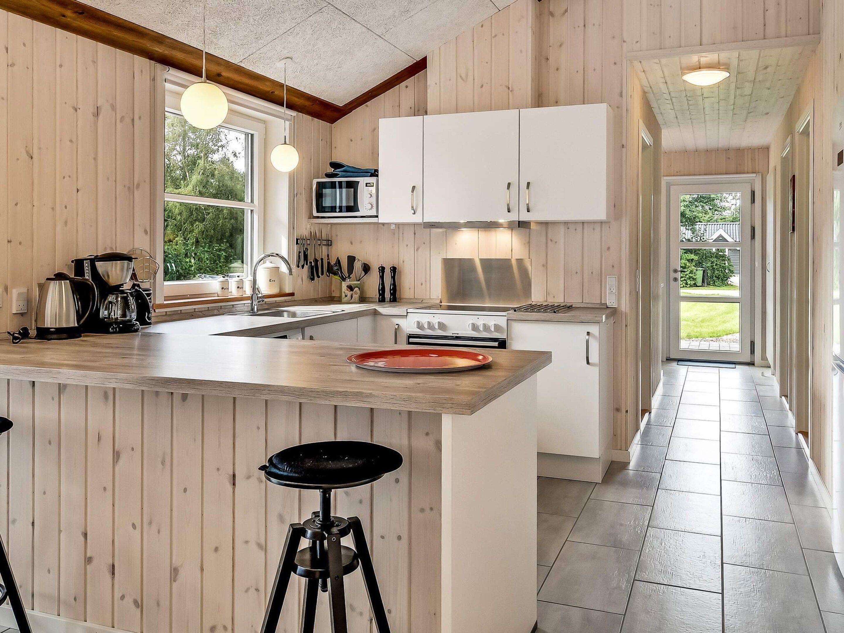 A modern kitchen with wooden paneling, a large island with stools, a stove, and a microwave.