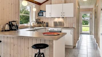 A modern kitchen with wooden paneling, a large island with stools, a stove, and a microwave.