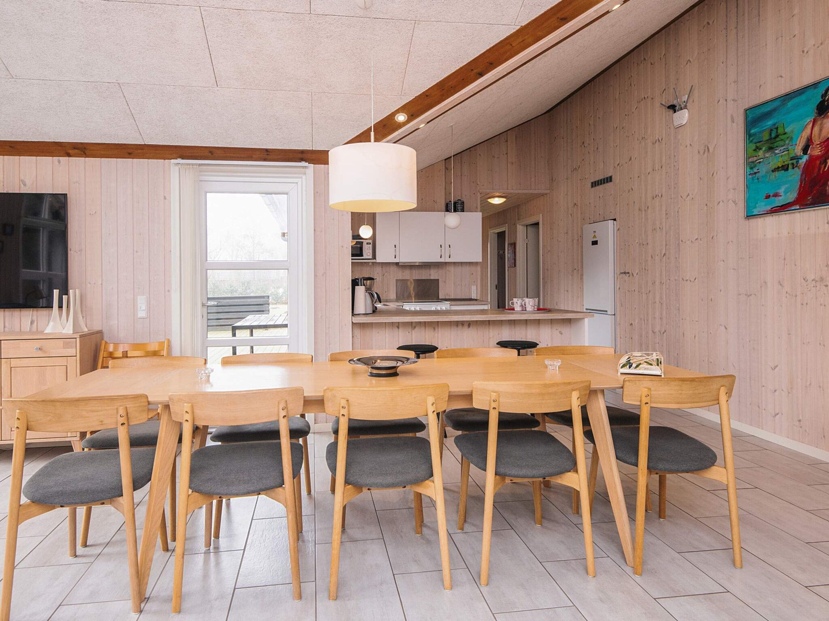 A modern kitchen with wooden cabinets, a dining area with a large table and chairs, and a hanging light fixture.