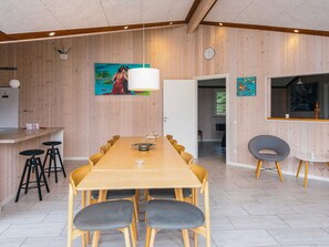 Un comedor moderno con una mesa y sillas de madera, una zona de bar con taburetes y vistas a otra habitación.