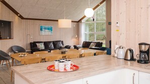 A cozy living room with a wooden ceiling, a large window, a sofa, and a dining table with chairs. - 4 Star Holiday Home in Oksbol (Oksbol)