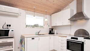 A modern kitchen with white cabinets, a built-in oven, a microwave, and a coffee maker. - Modernized Seaside Retreat-by Traum (Lokken)