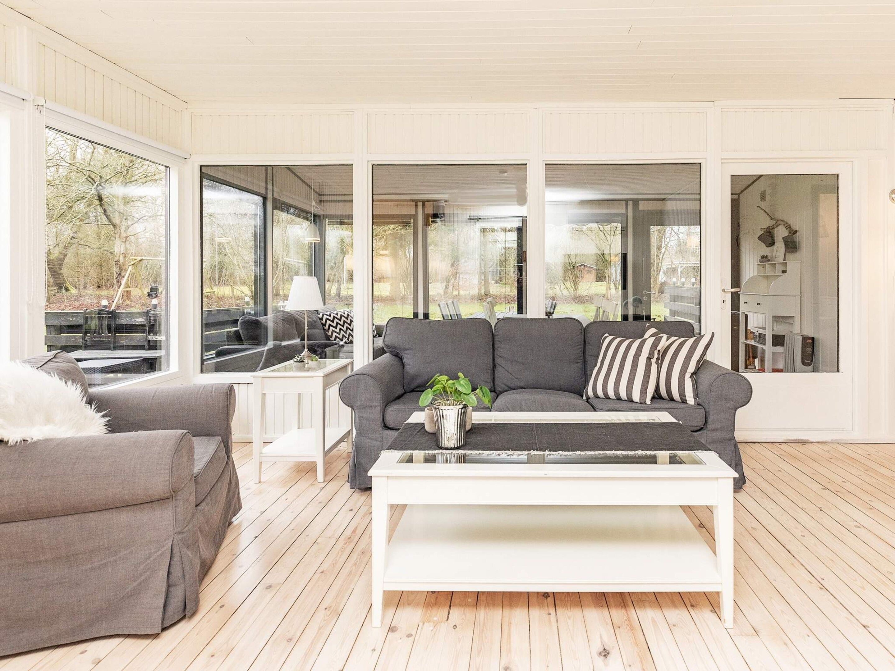 Una sala moderna con un sofá gris, una mesa de centro blanca y un sillón gris. Amplias ventanas ofrecen vistas al exterior.