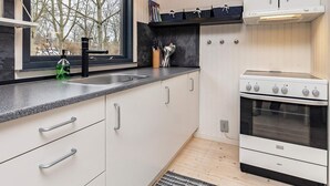 A modern kitchen with white cabinets, a black countertop, a built-in oven, and a window with a view of trees. - Secluded Forest Retreat-by Traum (Roslev)