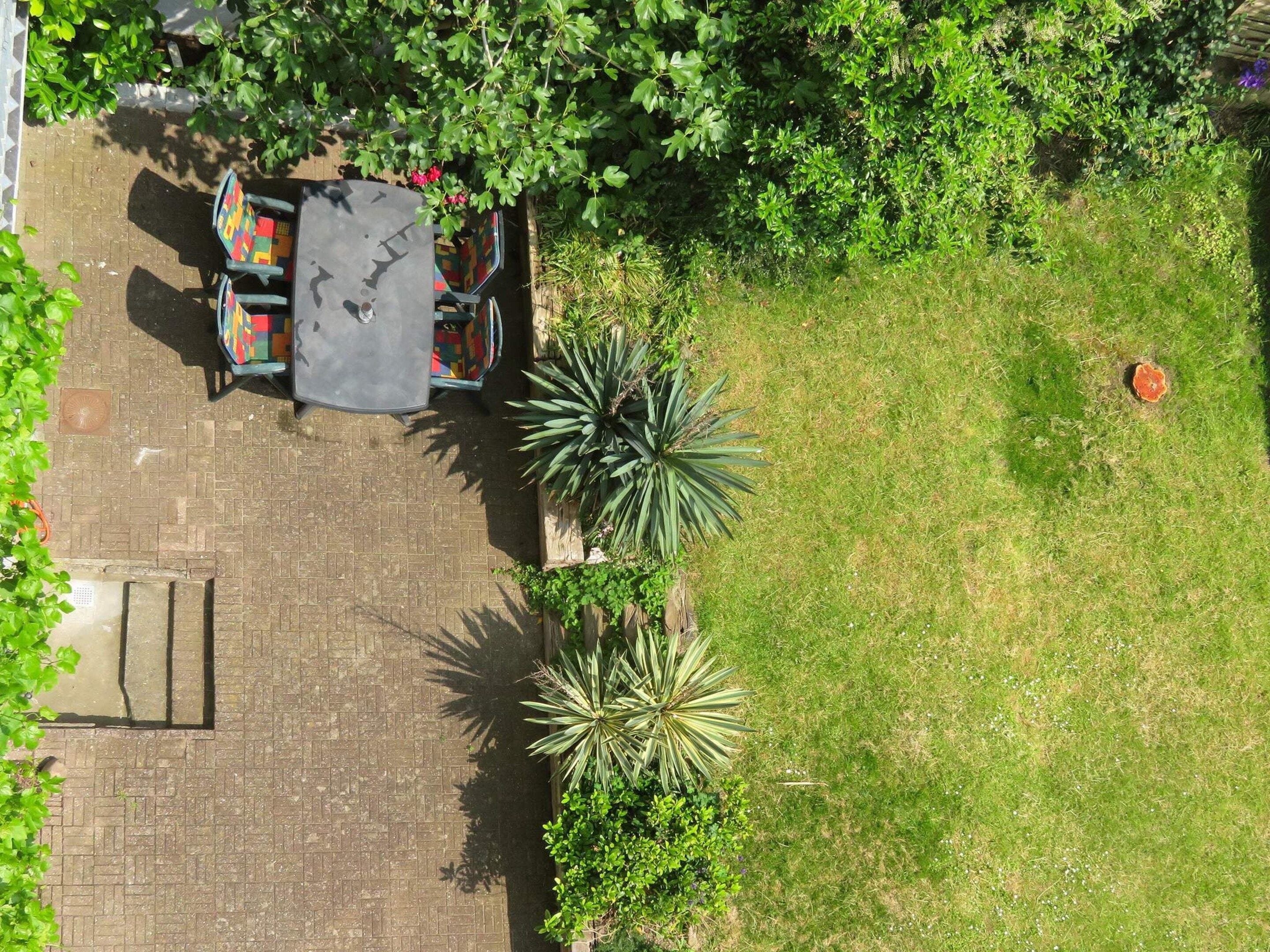 A patio area with a table and chairs, surrounded by greenery and a brick pathway.