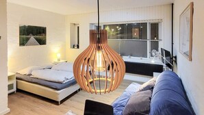 A modern bedroom with a bed, a sofa, a desk, and a hanging light fixture.