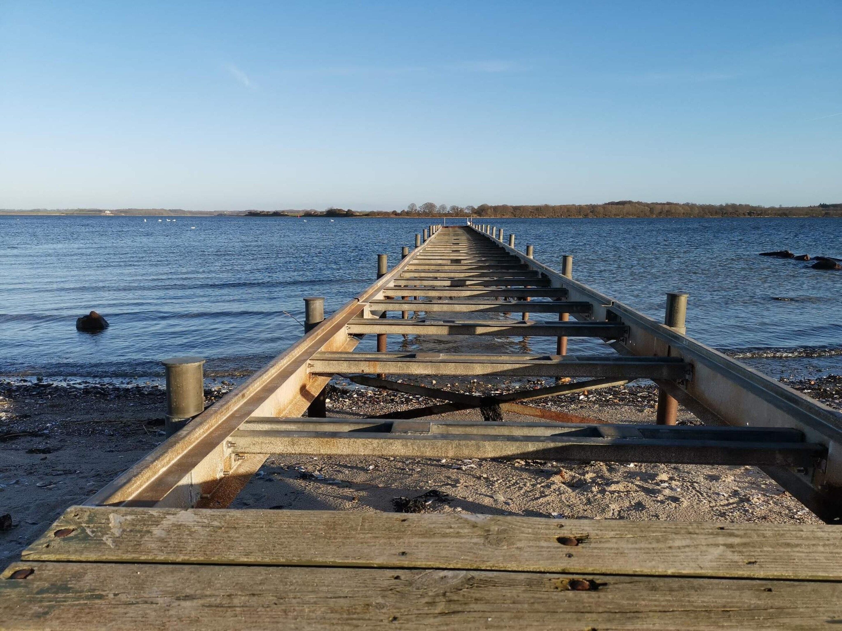 Un muelle de madera que se adentra en una masa de agua bajo un cielo despejado.