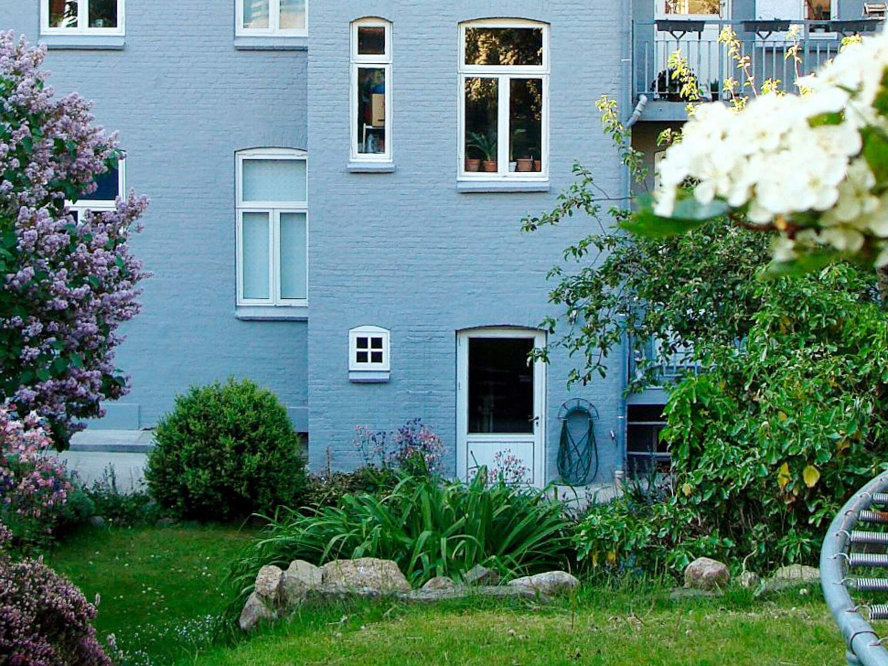 Un edificio de dos pisos con fachada azul, varias ventanas y una puerta pequeña.