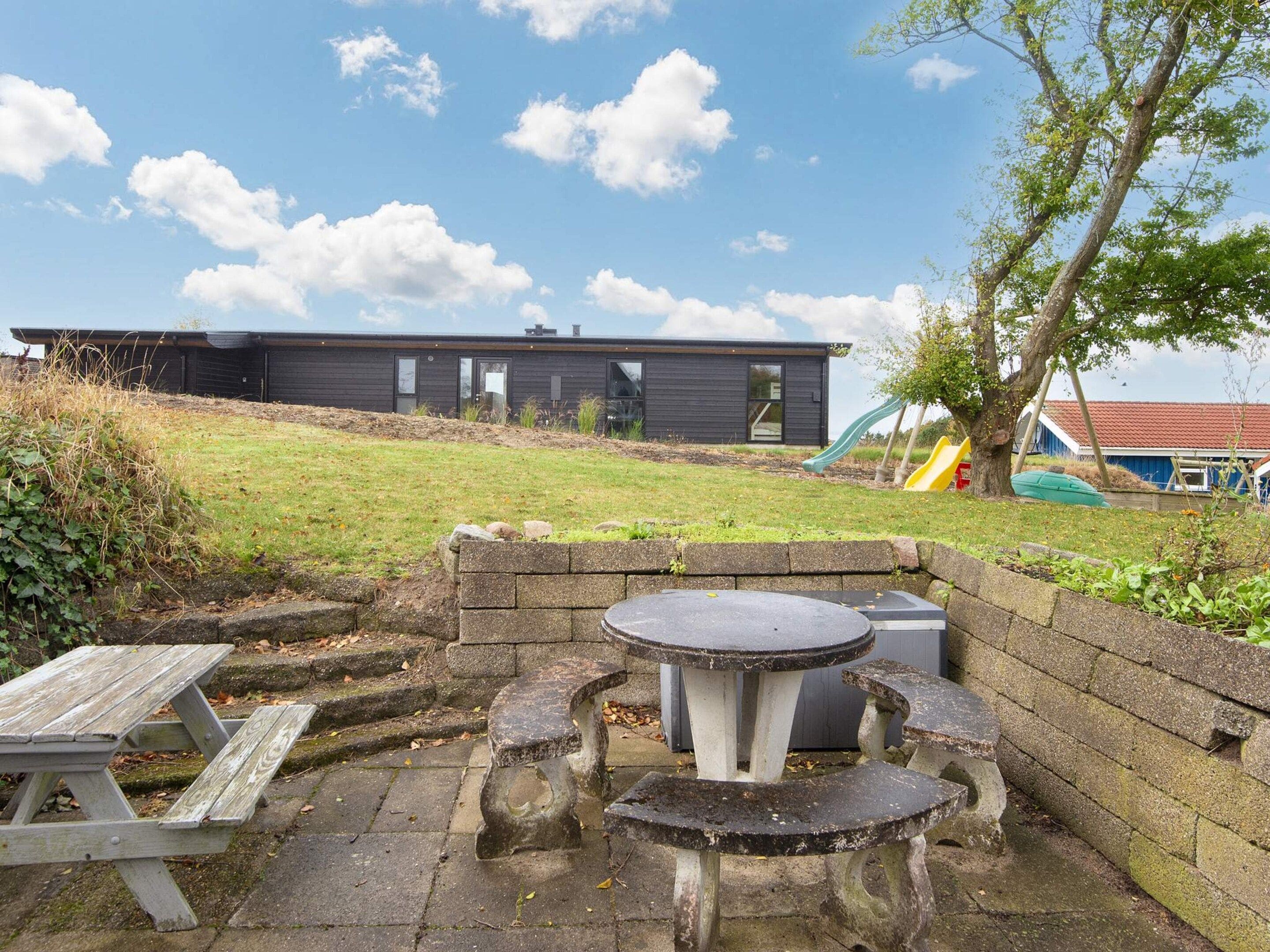 A picnic area with a table and benches, a slide, and a building in the background.