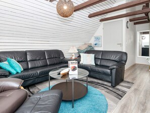 A modern living room with a black leather sofa, a glass coffee table, and a blue rug.