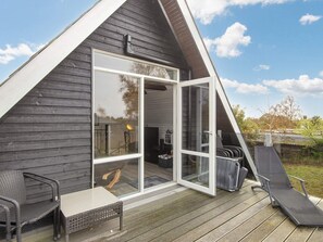 Um chalé em formato de A com porta de vidro, um deck com móveis de exterior e céu claro.