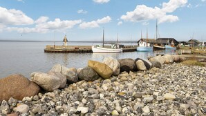 Kallioinen rantaviiva, jossa laituriin on ankkuroitu kalastusaluksia, majakka ja olkikatteinen rakennus.