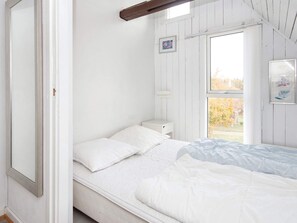 A white bedroom with a bed, a nightstand, and a window with a view of trees.