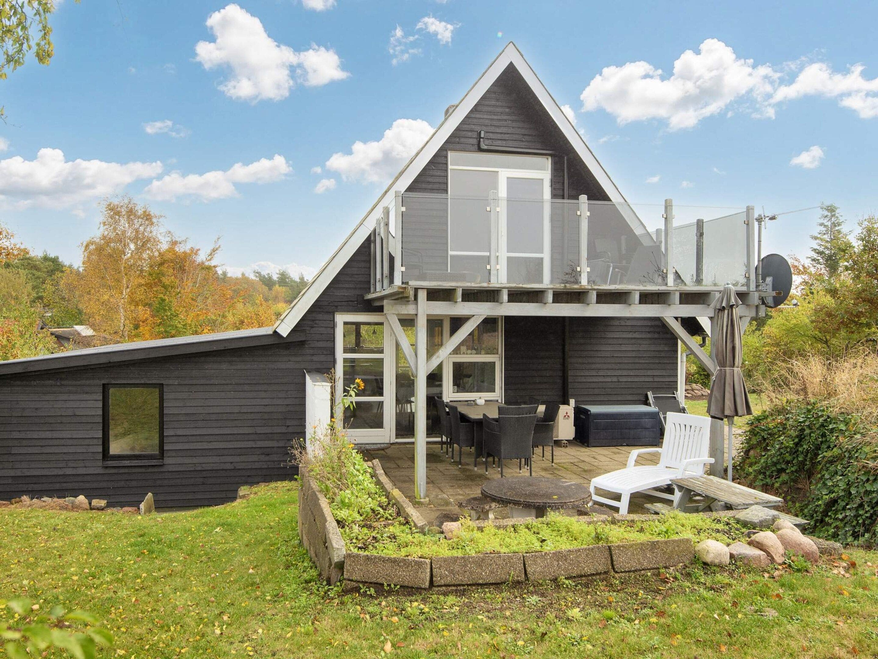 Ein modernes Haus mit Balkon, Sitzgelegenheit im Freien und einem Garten.